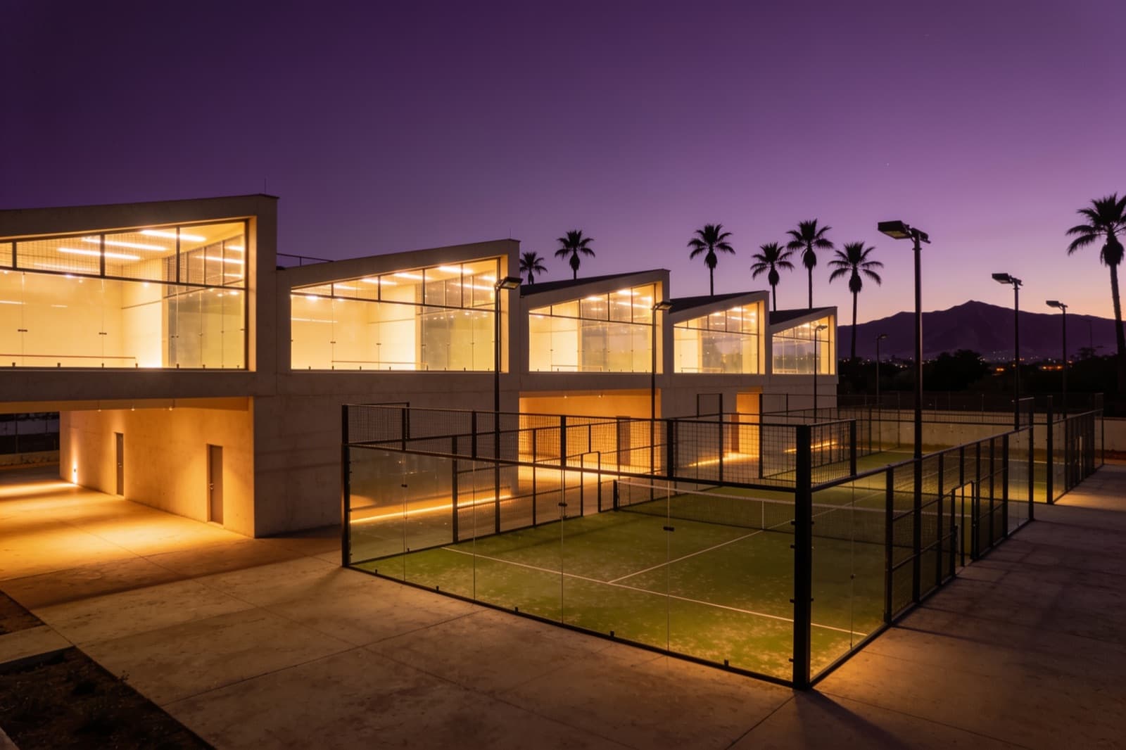 Club de pádel al anochecer, con las pistas de cristal iluminadas por dentro